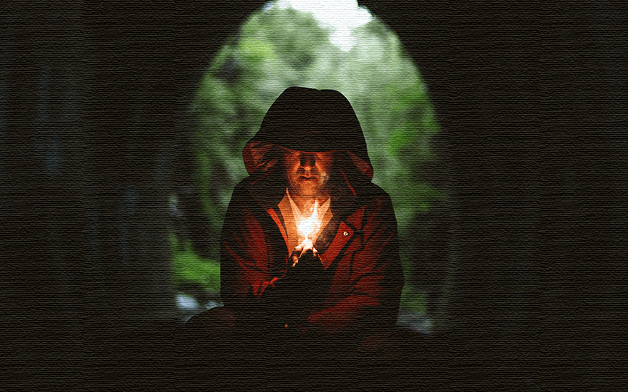 Image of a man with a lit match, squatting in a dark cave